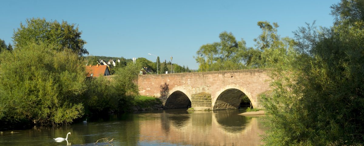 Blick über den Main auf eine alte rote Brücke im Landkreis Bad Kissingen, wie für dich gemacht