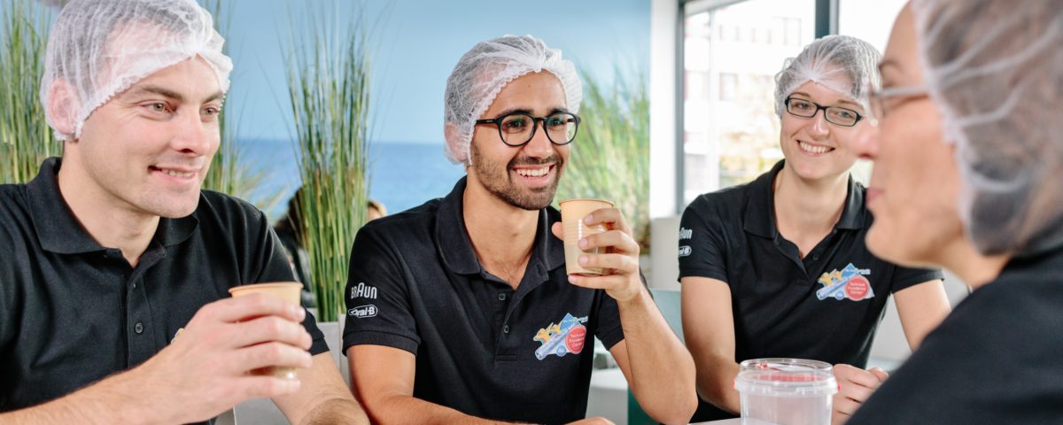 Four employees of Procter & Gamble GmbH in Marktheidenfeld with hair protection and cups in hand