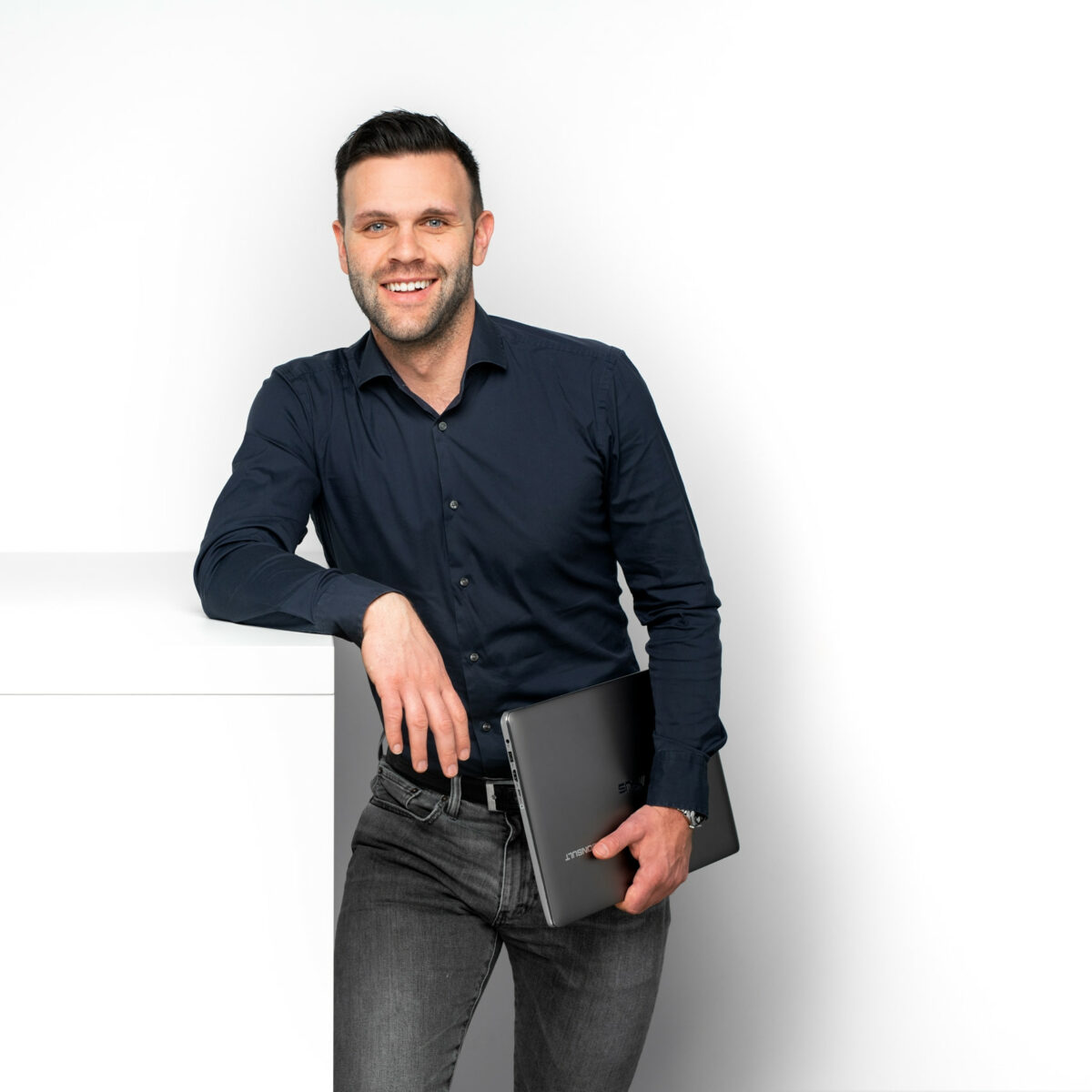 lächelnder Mitarbeiter von Baurconsult in blauem Hemd mit Laptop in der Hand in Hassfurt