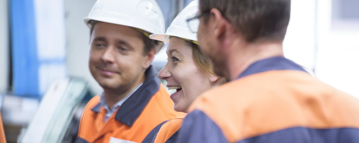 Drei Mitarbeiter in orangenen Warnwesten der Firma Franken Guss GmbH in Kitzingen unterhalten sich