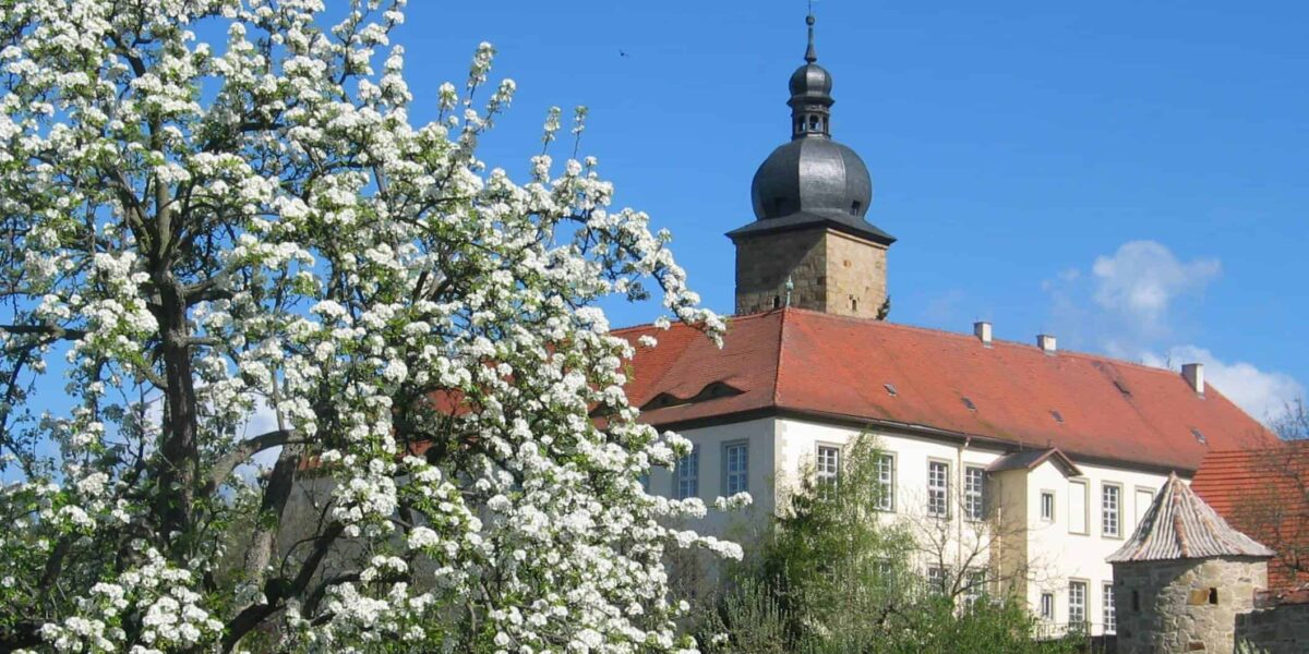 Sonniger Frühlingstag mit blühenden Bäumen und Blick auf ein Schloss im Landkreis Hassberge